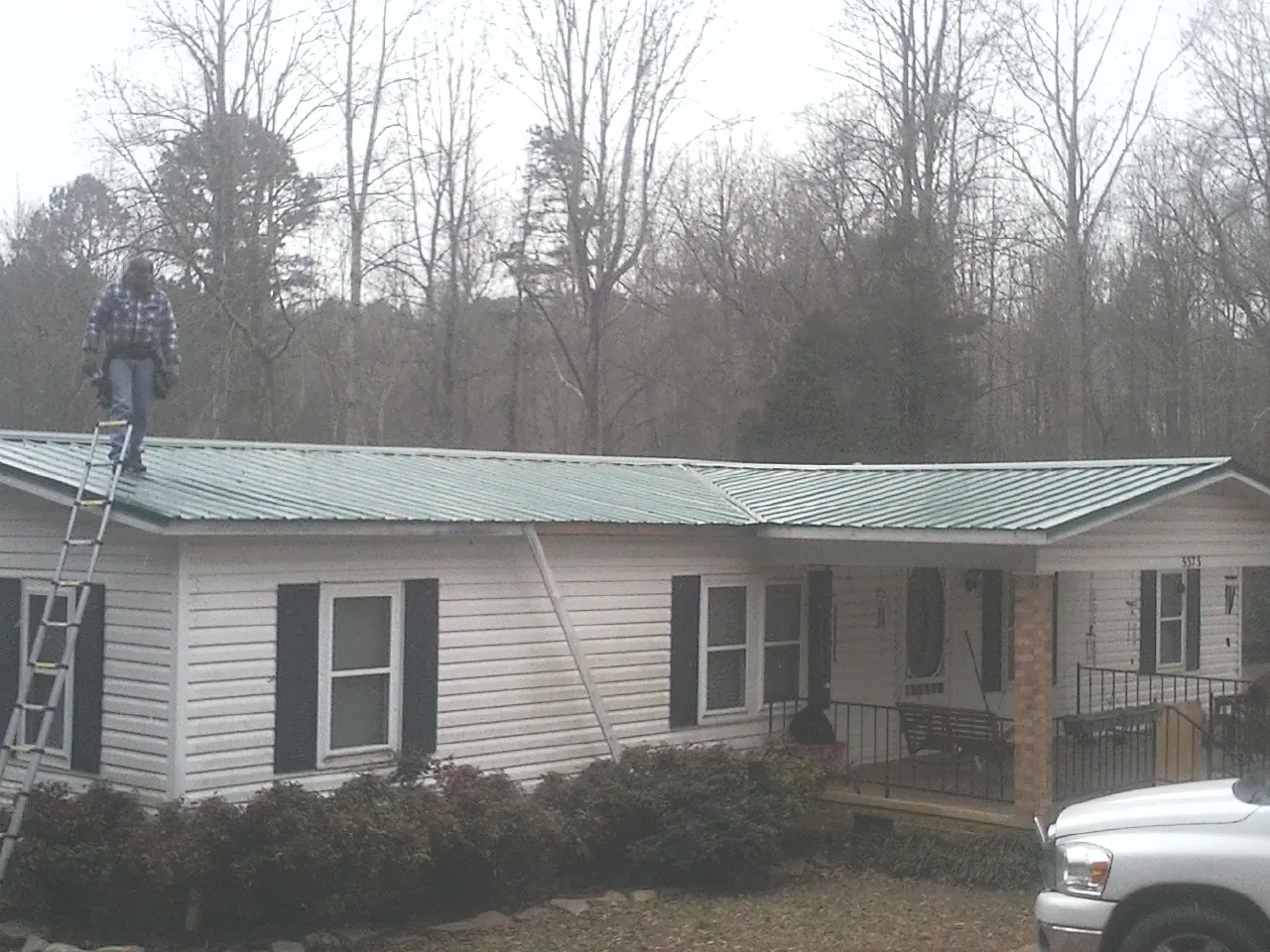 Worker on a ladder beside a new green metal roof on a ranch home in Newark Valley