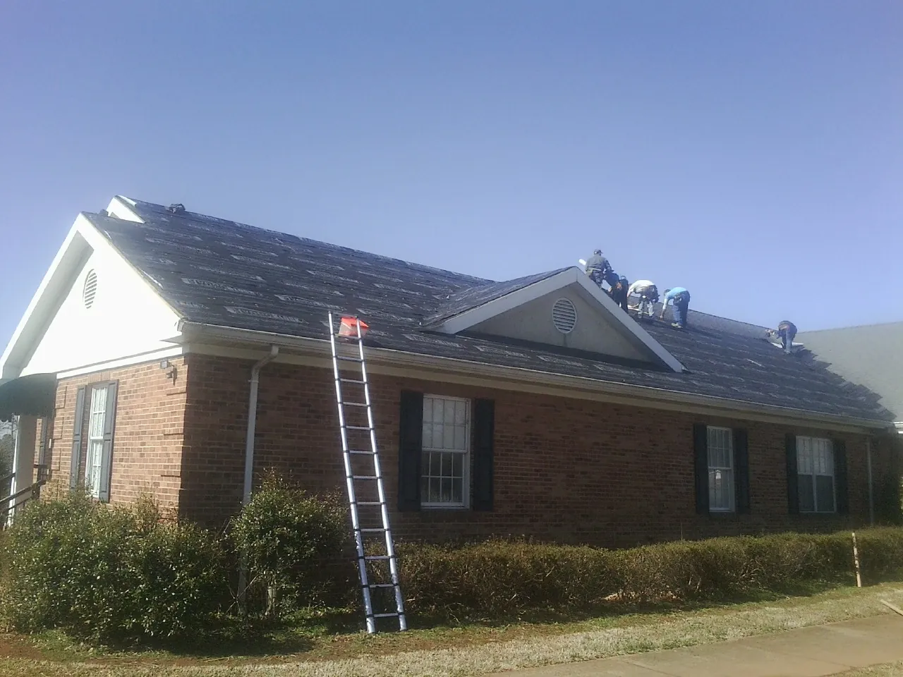 Crew tearing shingles off a brick ranch roof with a ladder set — Emergency Roof Repair work by our crew in Newark Valley
