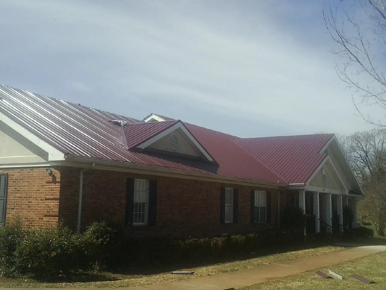Red metal roof with gabled entries on a long brick building, from a Hail Damage Roof Repair job in Newark Valley