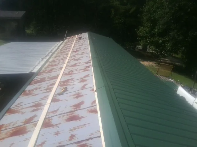 Old rusted panels beside newly installed green metal roofing — Wind Damage Roof Repair by Roofing Brothers in Newark Valley