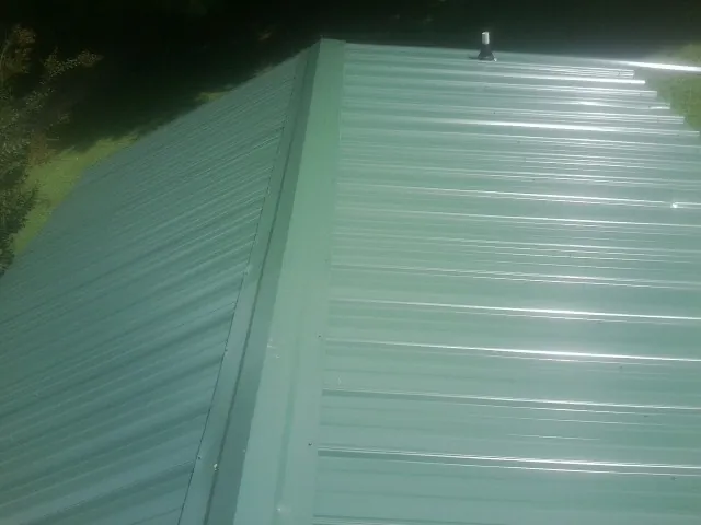 New green metal panels meeting at the ridge of a roof — Flat Roof Repair work by our crew in Newark Valley