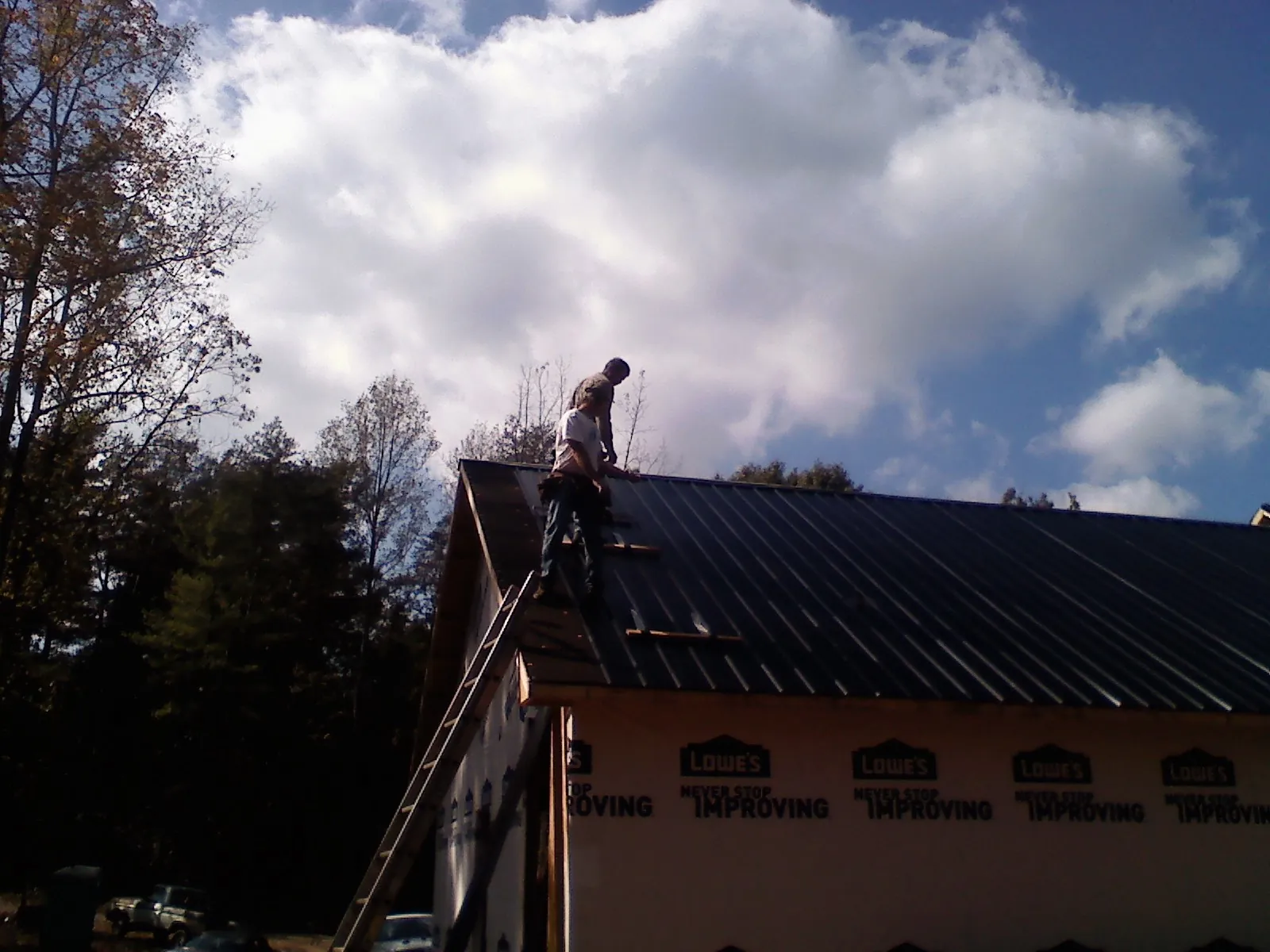 Roofer fastening dark metal panels high against a cloudy sky, from a Roof Inspection job in Newark Valley