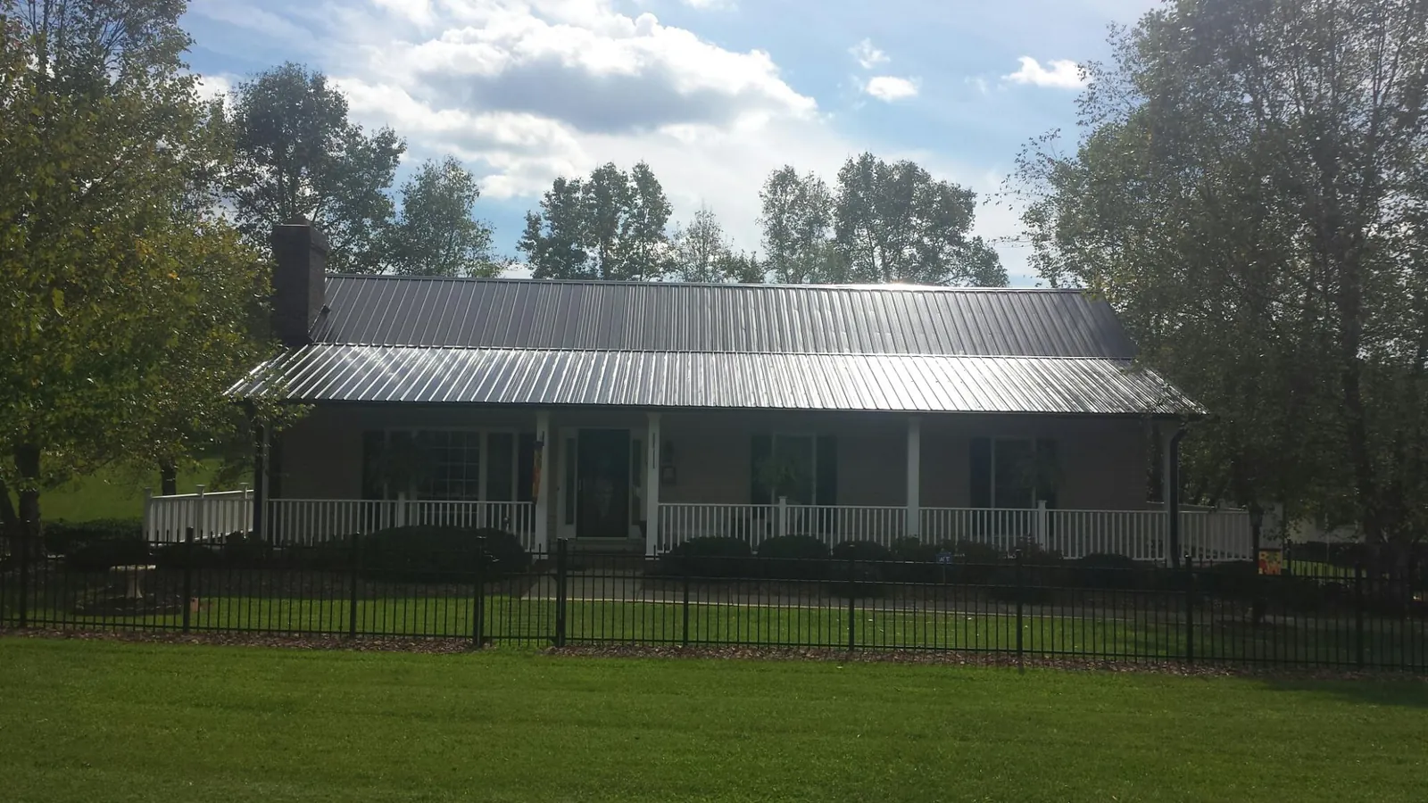 Gray metal roof on a brick ranch with a full width front porch — Gutter Guard Installation work by our crew in Newark Valley