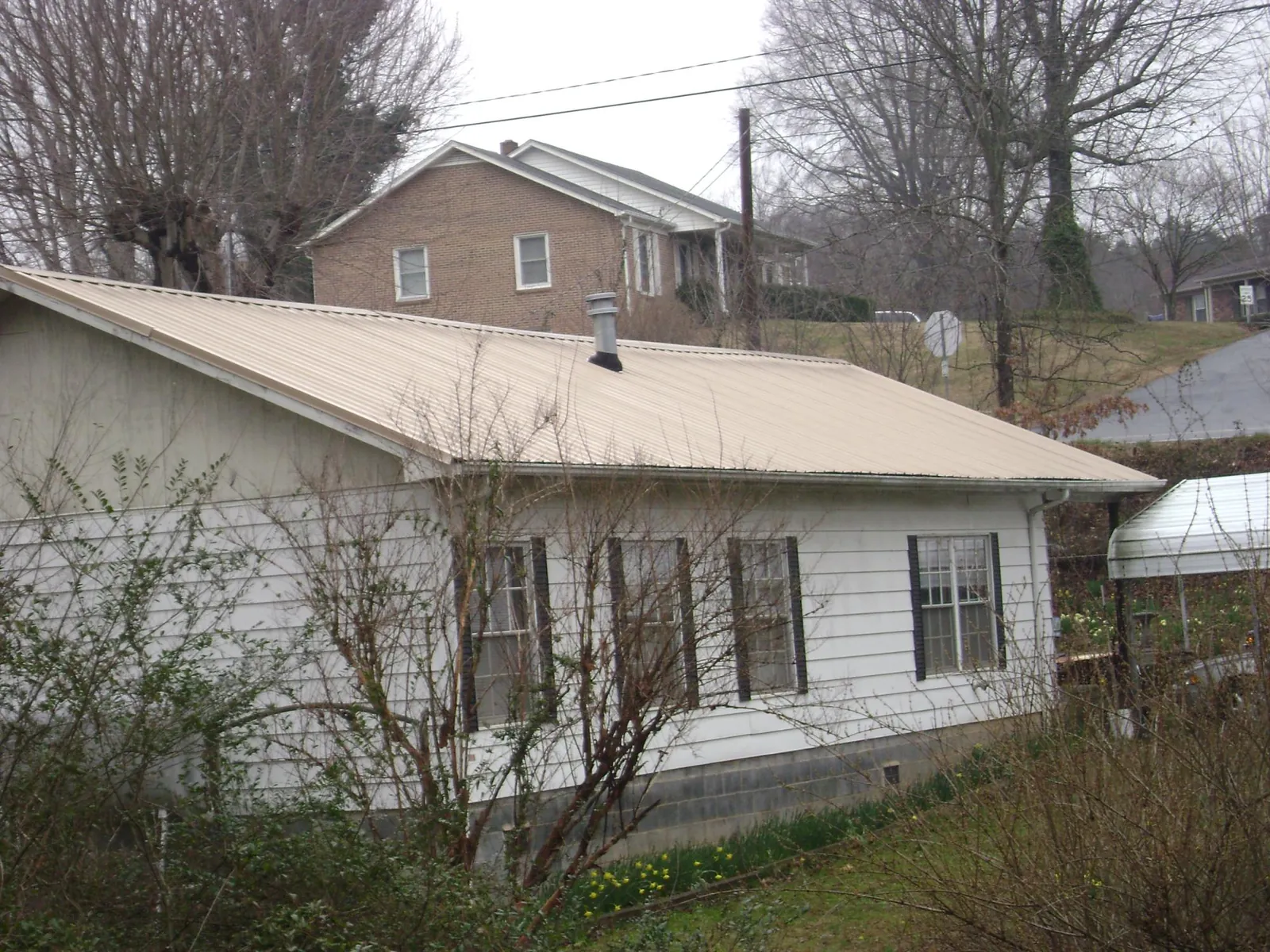 Tan metal roof on a white sided house set into a hillside — Commercial Roofing by Roofing Brothers in Newark Valley