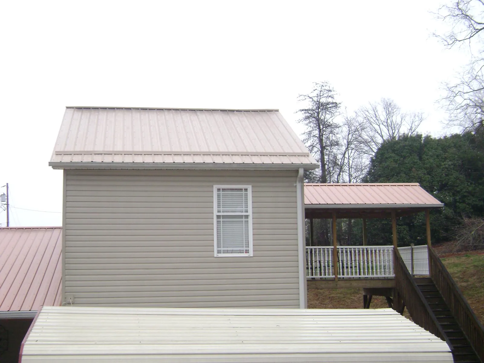 Tan metal roofs on a two story addition and attached porch, from a Roof Replacement job in Newark Valley